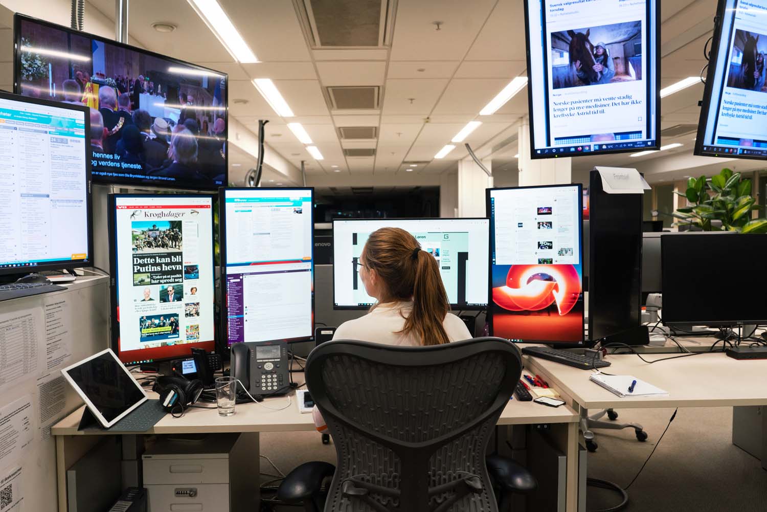 En kvinne sitter foran mange skjermer i et redaksjonslokale
