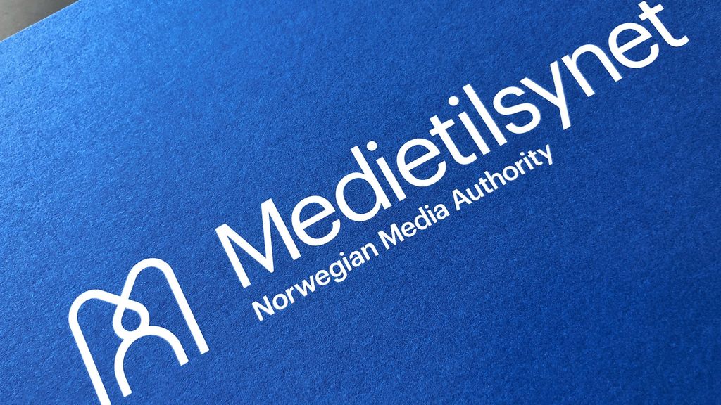 Medietilsynets logo i hvitt på blå bakgrunn. Foto.