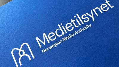 Medietilsynets logo i hvitt på blå bakgrunn. Foto.