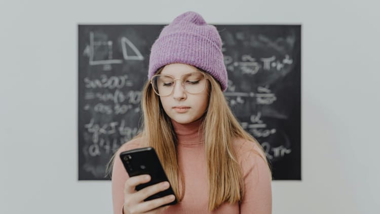 En jente ser på mobilen sin foran en tavle