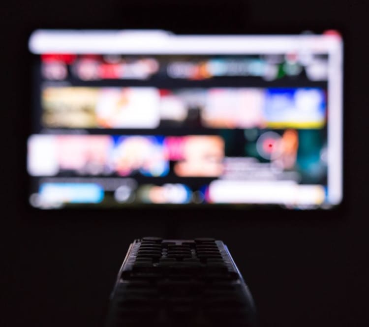 Nærbilde av fjernkontroll med uskarp tv-skjerm i bakgrunnen.