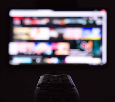 Nærbilde av fjernkontroll med uskarp tv-skjerm i bakgrunnen.