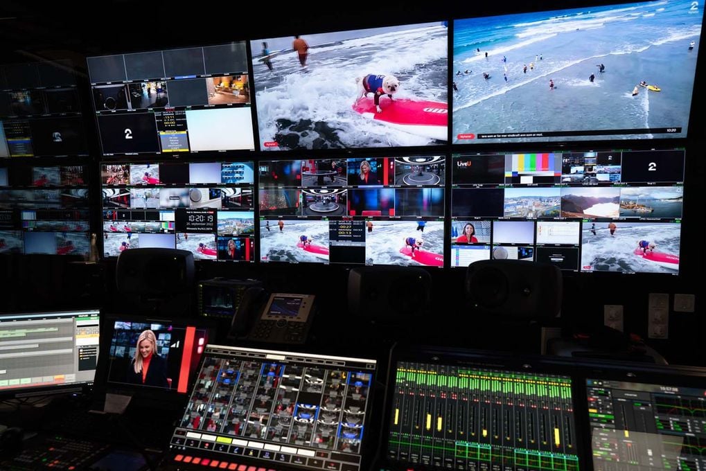 Kontrollpanel for tv-regi og mange skjermer med forskjellige bilder. Rommet er mørkt, men skjermene lyser opp.
