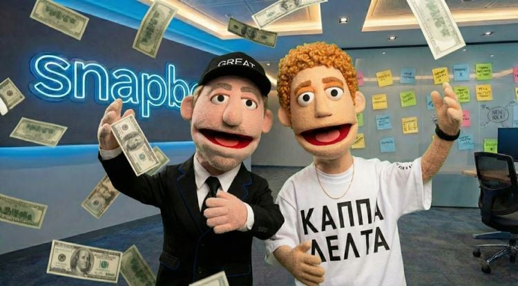 To dukkelignende figurer står i et moderne kontorlokale med en blå neonlyslogo i bakgrunnen der det står «Snapb». Den ene figuren har på seg svart dress og caps, den andre har krøllete hår og hvit T-skjorte med gresk skrift. Begge smiler og gestikulerer mot kamera. Rundt dem faller amerikanske dollarsedler fra taket. På veggen bak dem henger fargerike post-it-lapper, og et kontorområde med stol og skrivebord er synlig i bakgrunnen.