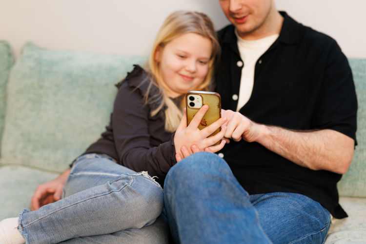 Barn og forelder sitter i en sofa og ser på en smarttelefon