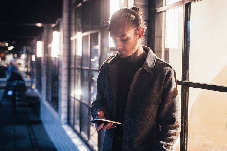 Ung mann står utenfor en bygning og leser nyheter på mobilen.