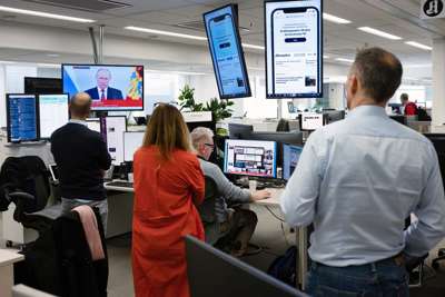 Bilde fra redaksjon. Noen sitter ved arbeidsplasser med tastatur og skjermer mens noen står rundt desken.