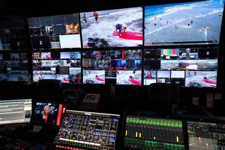Regi-panel og tv-skjermer. Knapper og spaker i forgrunnen og store skjermer med mange forskjellige bilder på veggen bak.