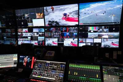Regi-panel og tv-skjermer. Knapper og spaker i forgrunnen og store skjermer med mange forskjellige bilder på veggen bak.