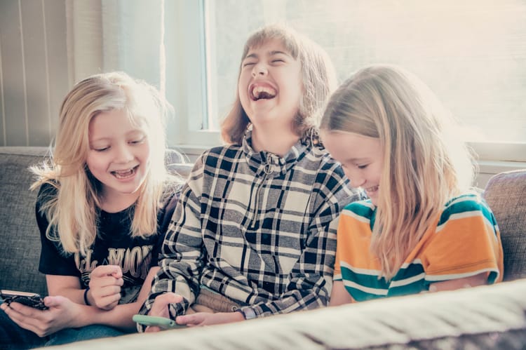 Tre jenter i 10  -12-årsalderen ser på mobilene sine og ler. Foto Kine Jensen/ Medietilsynet