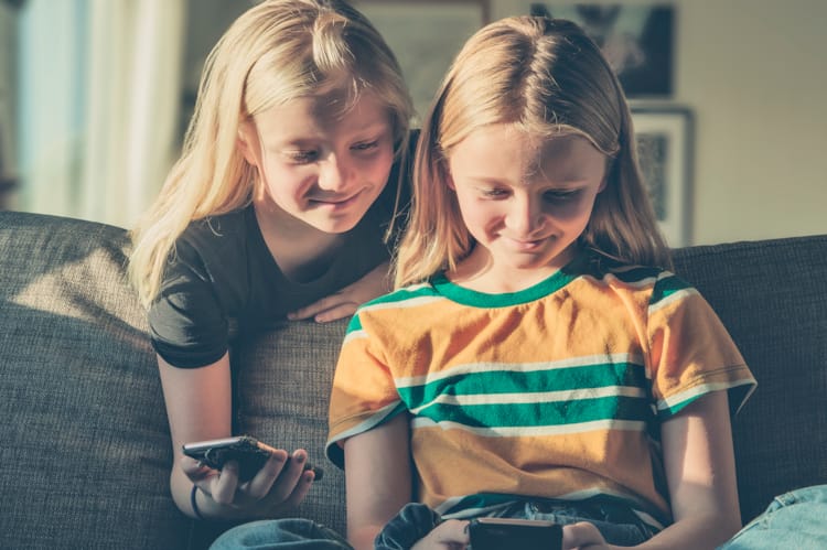 To jenter i 10-årsalderen sitter og ser på samme mobilskjerm. Foto Medietilsynet/Kine Jensen