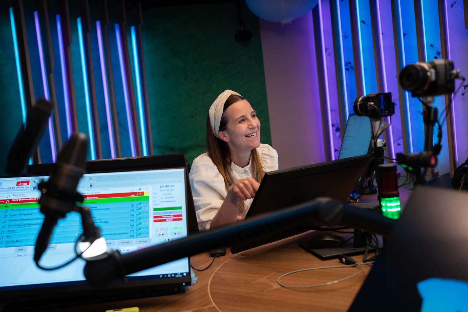 Radiostudio med skjermer, mikrofoner og en blid kvinnelig journalist. Foto Ketil Blom/ Medietilsynet