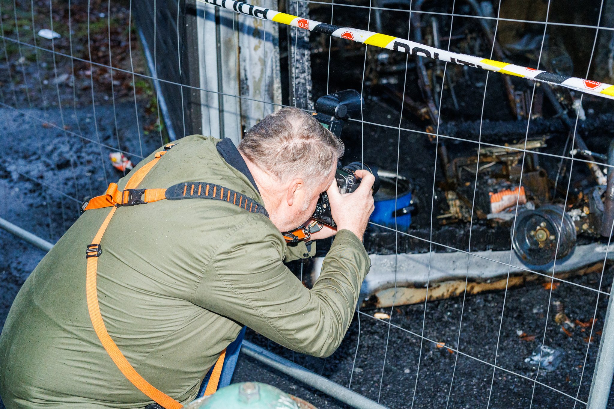 Fotograf dokumenterer brannskadet omr&aring;de bak gjerde med kamera.
