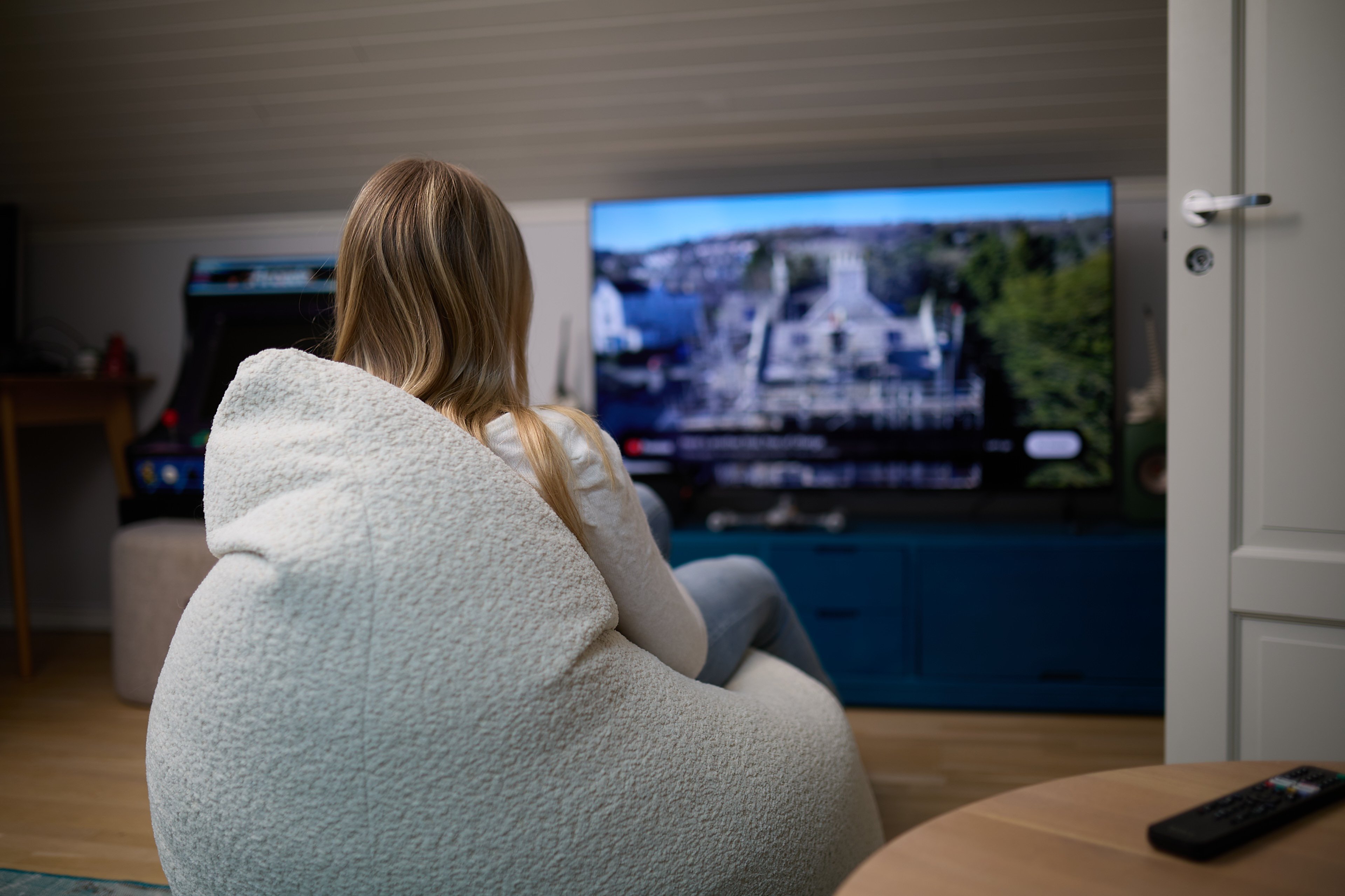 Person sitter i stol hjemme og ser p&aring; TV i stue.