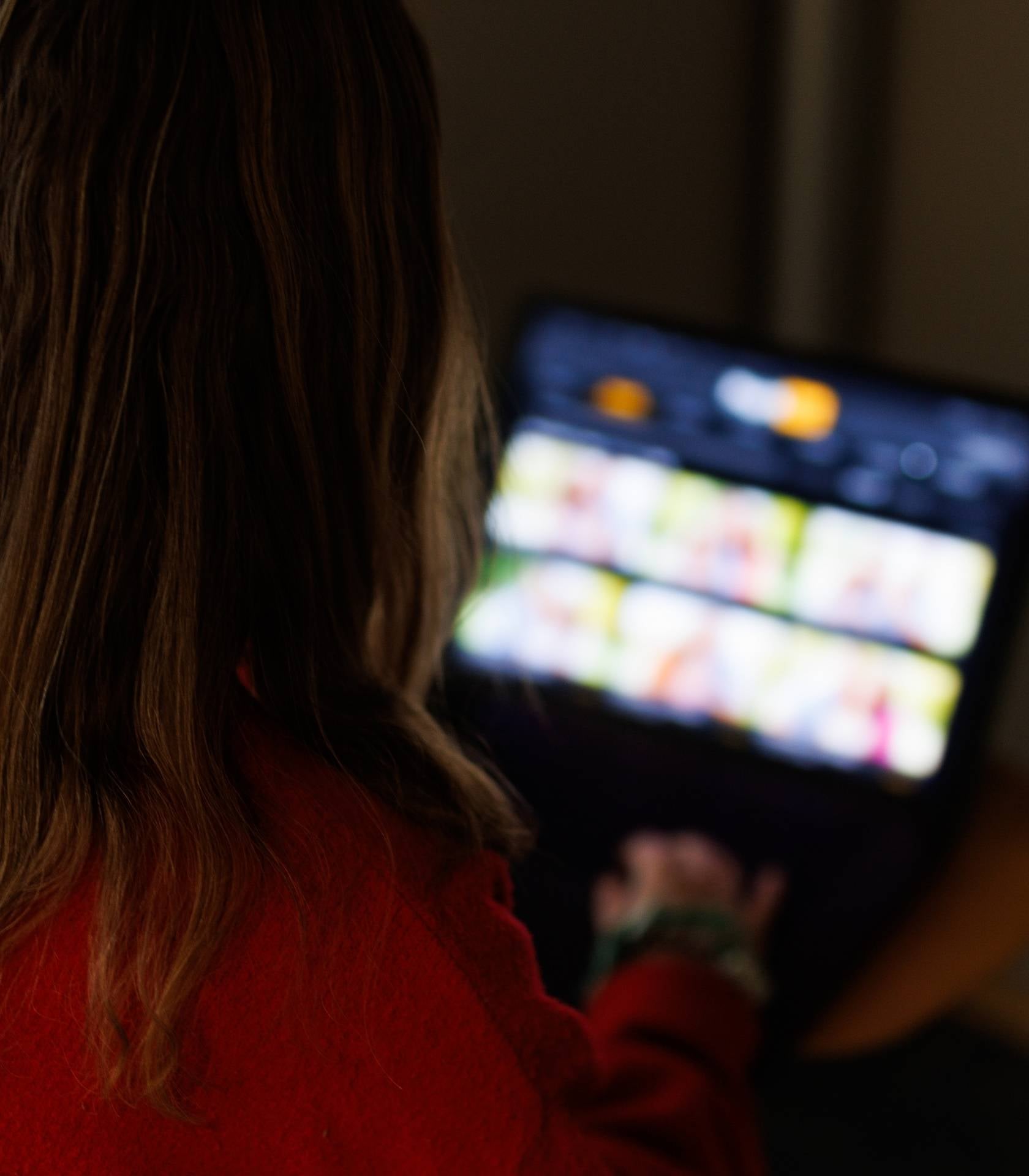 Person sitter i et mørkt rom og bruker et nettbrett med flere bilder eller innholdsfelt på skjermen.